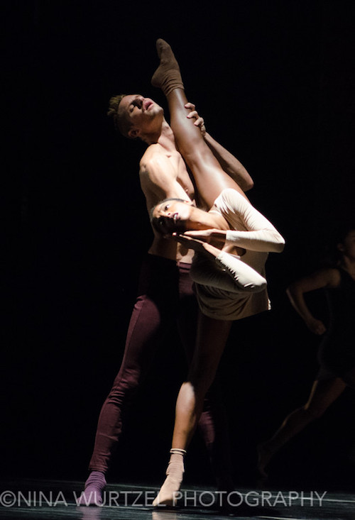 A male dancer holds his partner's knee as she executes a high penchee